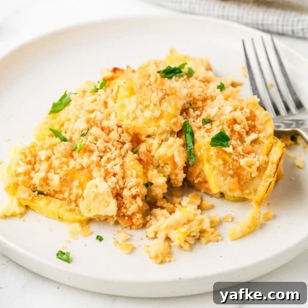 A serving of yellow squash casserole with a golden cracker topping on a white plate.
