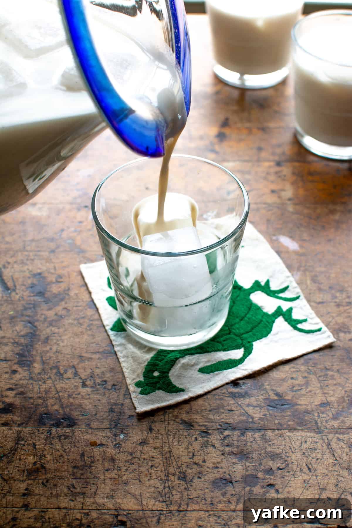 Authentic Creamy Mexican Horchata Recipe with Rice and Cinnamon 2 A pitcher with a blue rim pouring horchata into a glass filled with ice on a wood table.