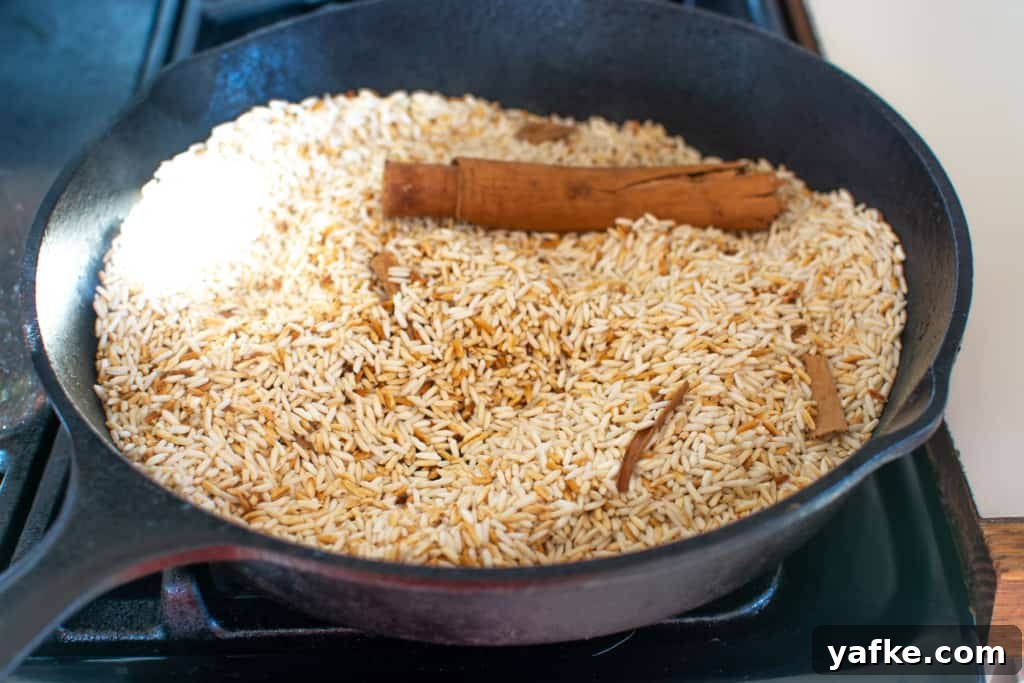 Authentic Creamy Mexican Horchata Recipe with Rice and Cinnamon 5 Jasmine rice and a stick of canela toasting in a black cast iron skillet on the stove top.