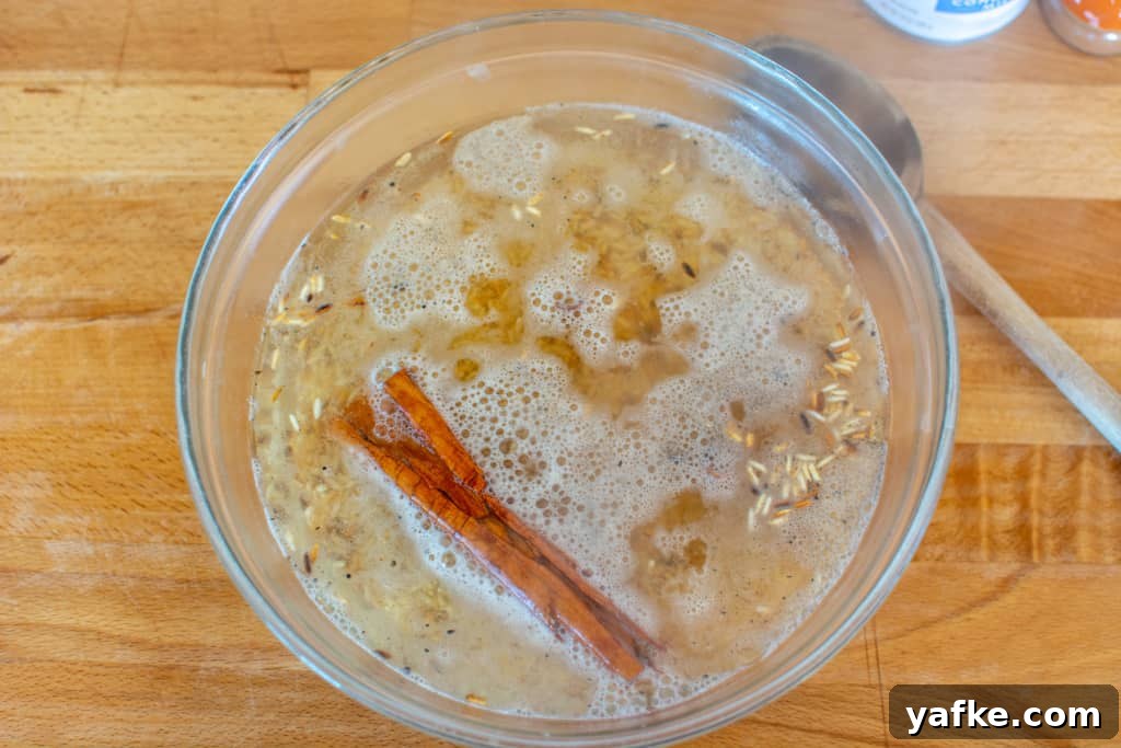 Authentic Creamy Mexican Horchata Recipe with Rice and Cinnamon 6 A glass bowl filled with toasted rice and a stick of canela topped with boiling water and a wood spoon next to it.