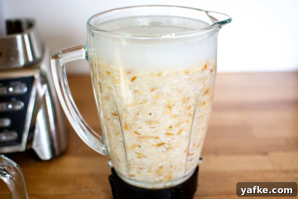 Authentic Creamy Mexican Horchata Recipe with Rice and Cinnamon 7 A glass carafe of a blender filled with toasted rice and water sitting on a wood counter next to the bottom of the blender.
