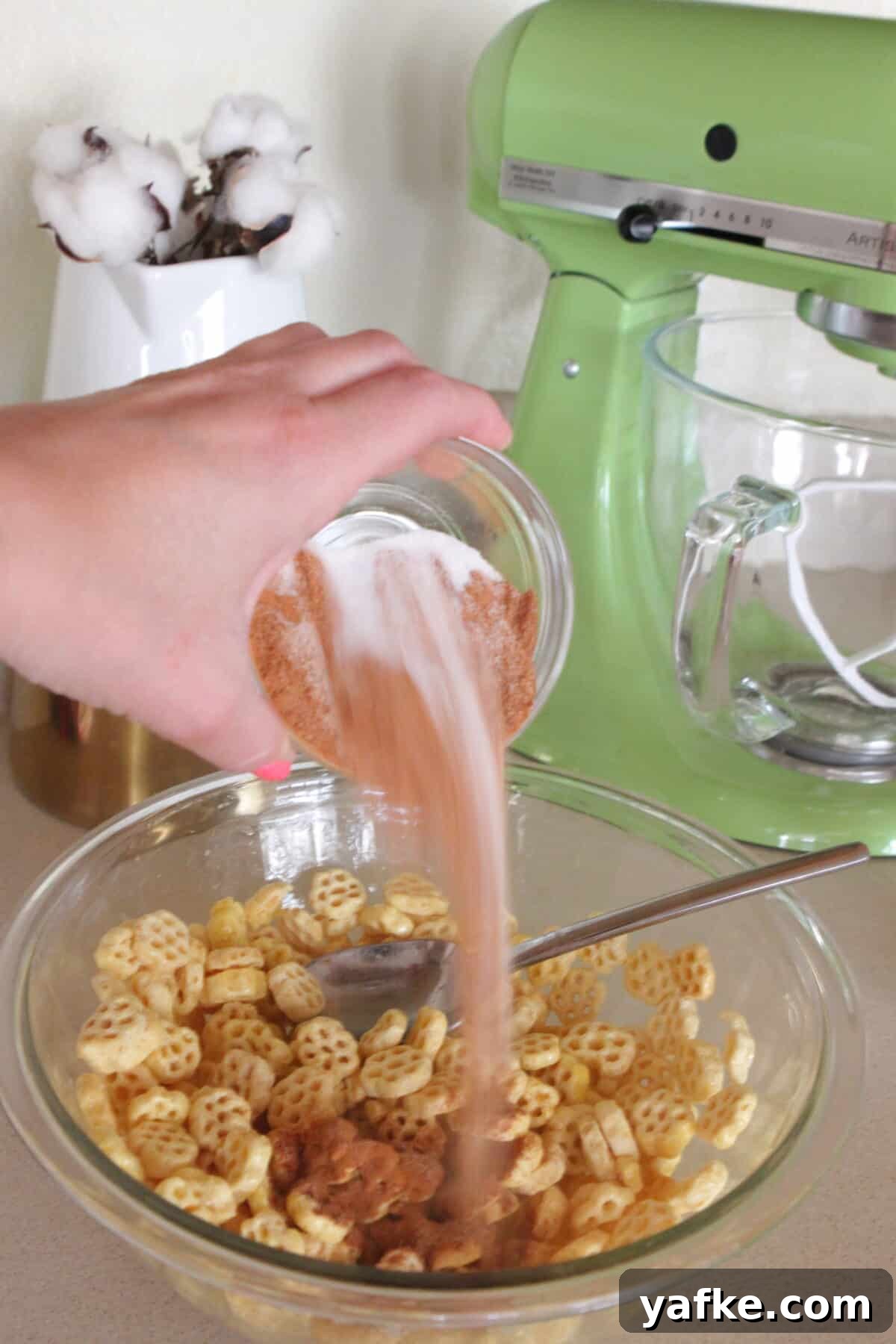 White Chocolate Churro Crunch Snack Mix Recipe 5 adding cinnamon sugar over cereal mixture in mixing bowl