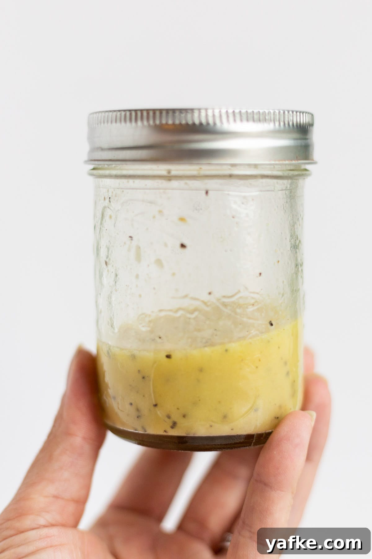 Salad dressing in a mason jar held up by a hand.