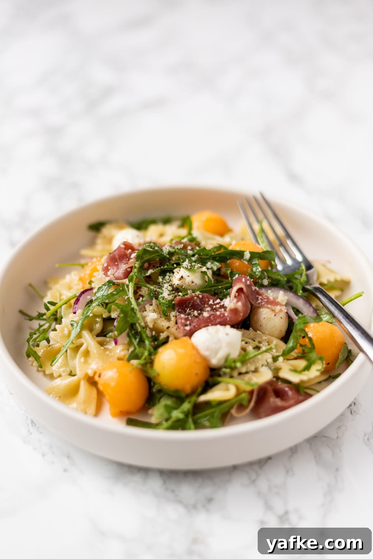 a side view of a plate of prosciutto melon pasta salad