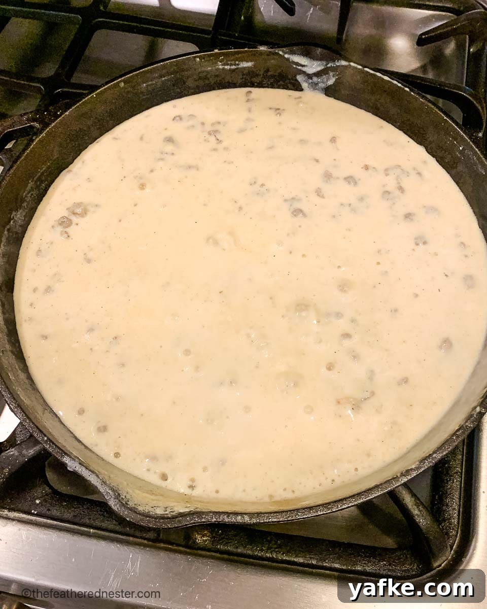 How to Make Homemade Sausage Gravy for Biscuits 5 a cast iron skillet of sausage and milk simmering on the stove.