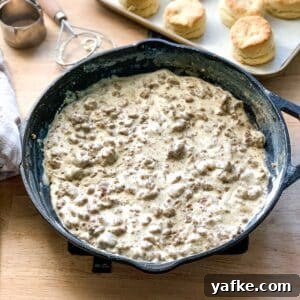 How to Make Homemade Sausage Gravy for Biscuits 7 a cast iron skillet of gravy sausage with a pan of biscuits in the background.