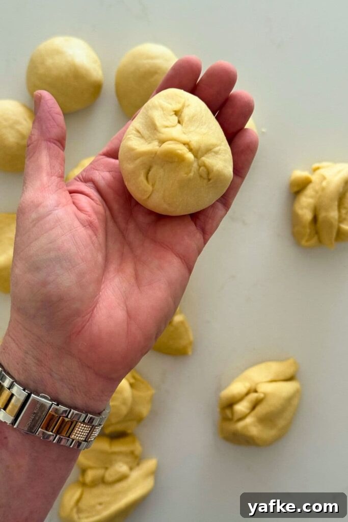 Fluffy Sourdough Discard Honey Butter Dinner Rolls 8 A hand holding a piece of sourdough honey butter roll dough.