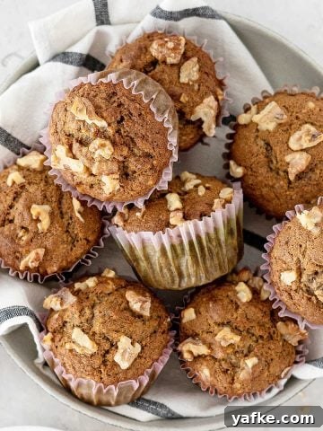 Close up of piled banana nut muffins on a striped cloth with a light grey background.