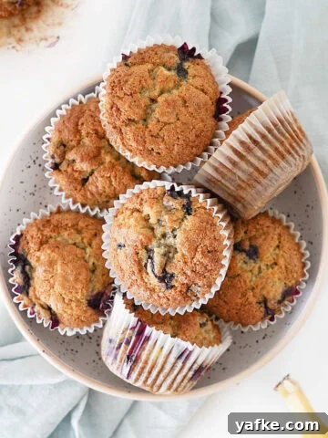 Close up of blueberry banana muffins in white paper liners. White surface, light blue cloth.