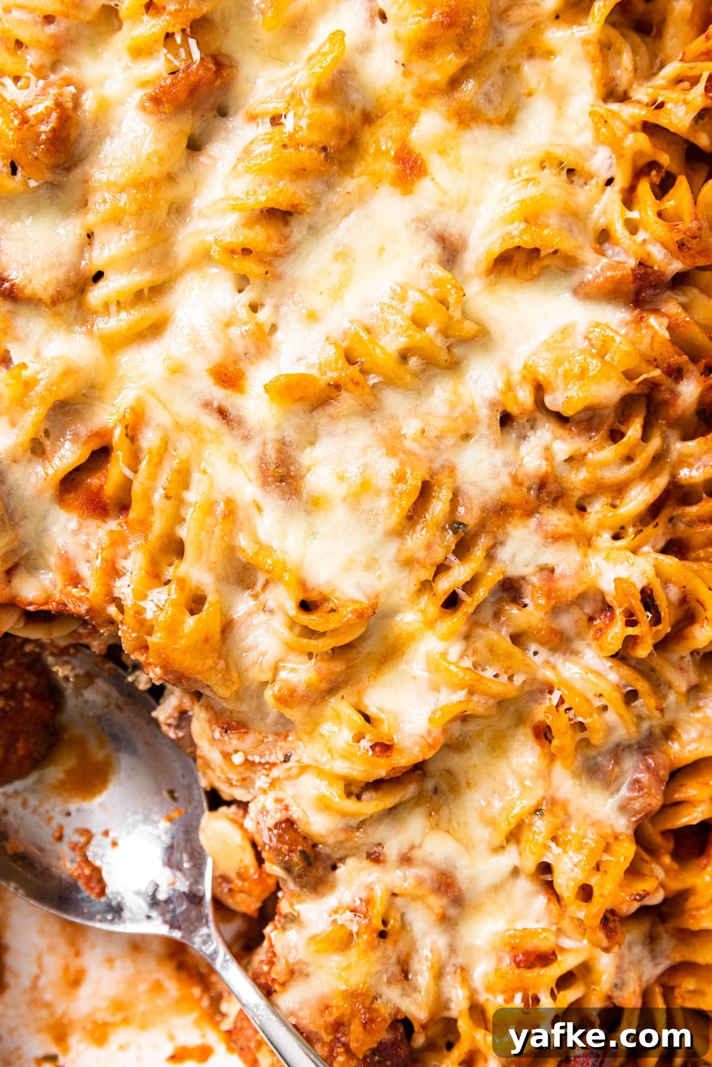 Cheesy Baked Rotini Casserole with Marinara and Mozzarella 3 Top down view of baked rotini casserole in baking dish with cheese all over the top with burnt crisp edges showing and spoon sitting in dish
