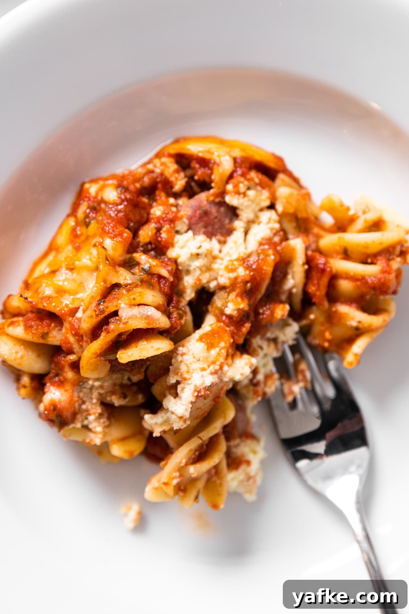 Cheesy Baked Rotini Casserole with Marinara and Mozzarella 5 Top down view of serving of baked rotini casserole sitting on white plate with fork getting a piece