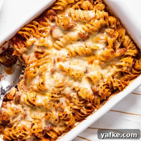 Cheesy Baked Rotini Casserole with Marinara and Mozzarella 6 Top down view of white baking dish filled with pasta with red sauce and cheese all over the top with spoon sitting in dish