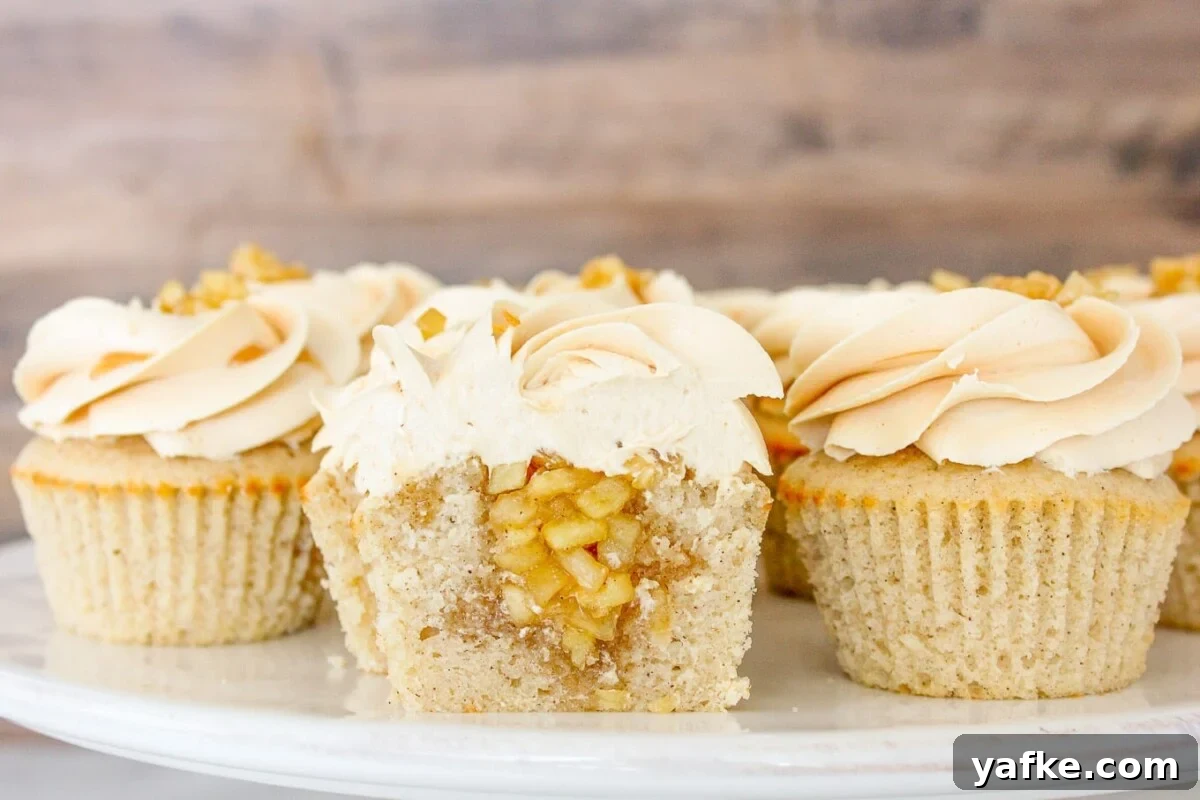 Caramel Apple Cupcakes Recipe with Salted Caramel Frosting 2 Cake stand full of caramel apple cupcakes one sliced in half to show apple filling.