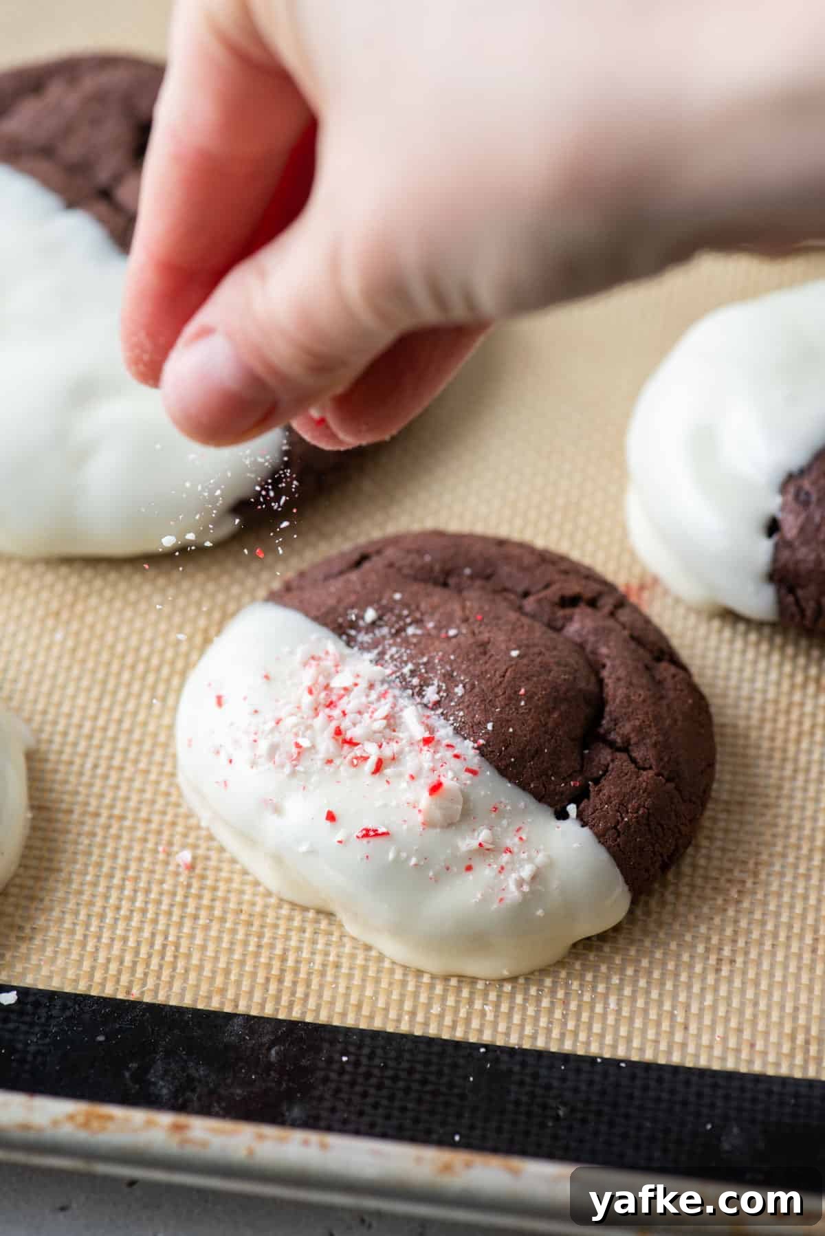 A hand sprinkling crushed candy canes over a cookie