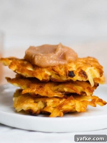 three latkes stacked on a plate with a dollop of applesauce