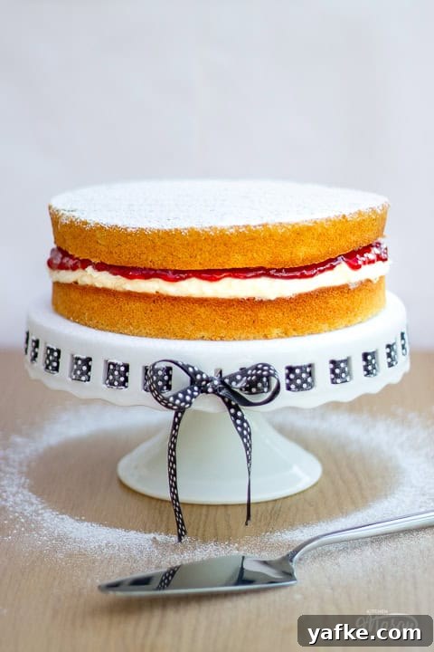 a Victoria sandwich cake on a cake stand dusted with icing sugar