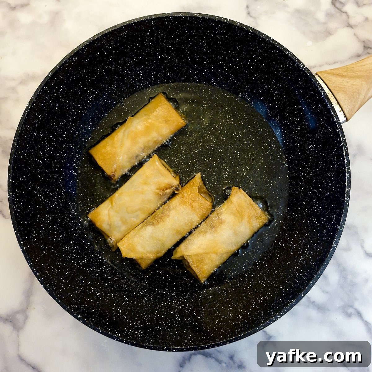 Crispy Prawn Spring Rolls Recipe with Sweet Chili Dip 12 4 spring rolls browning in oil in a frying pan.