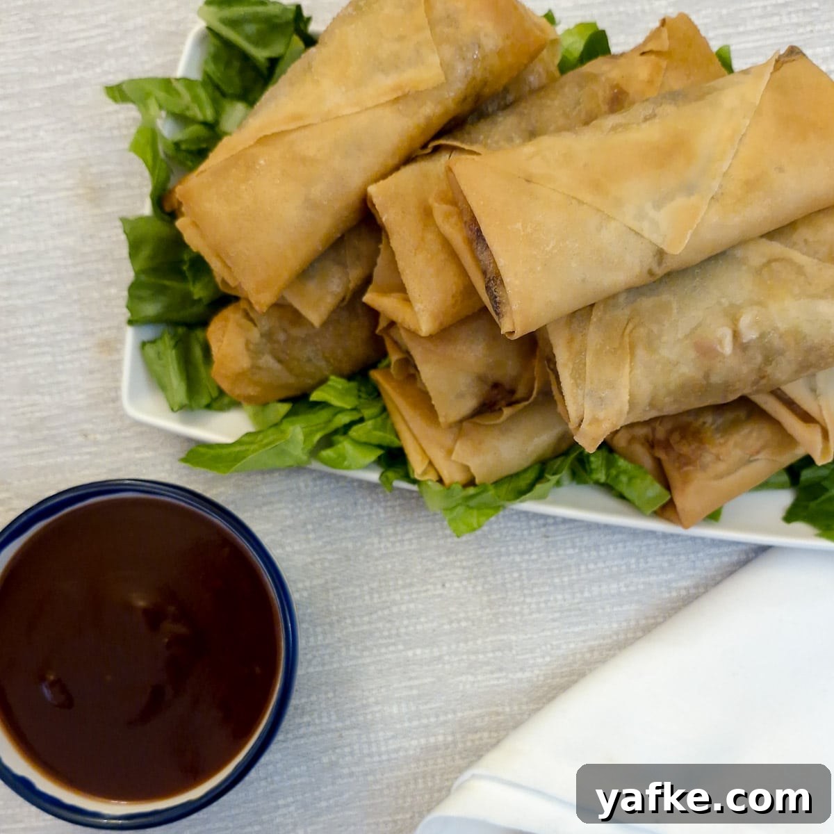 Crispy Prawn Spring Rolls Recipe with Sweet Chili Dip 2 A pile of crispy prawn spring rolls on a plate next to bowl of dipping sauce.