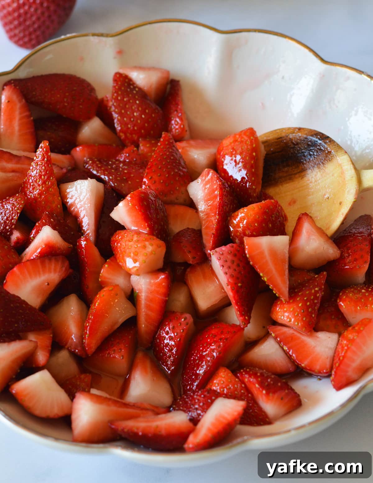 Macerated Strawberries Recipe with Lemon and Vanilla 2 a bowl of macerated strawberries with a wooden spoon in it.