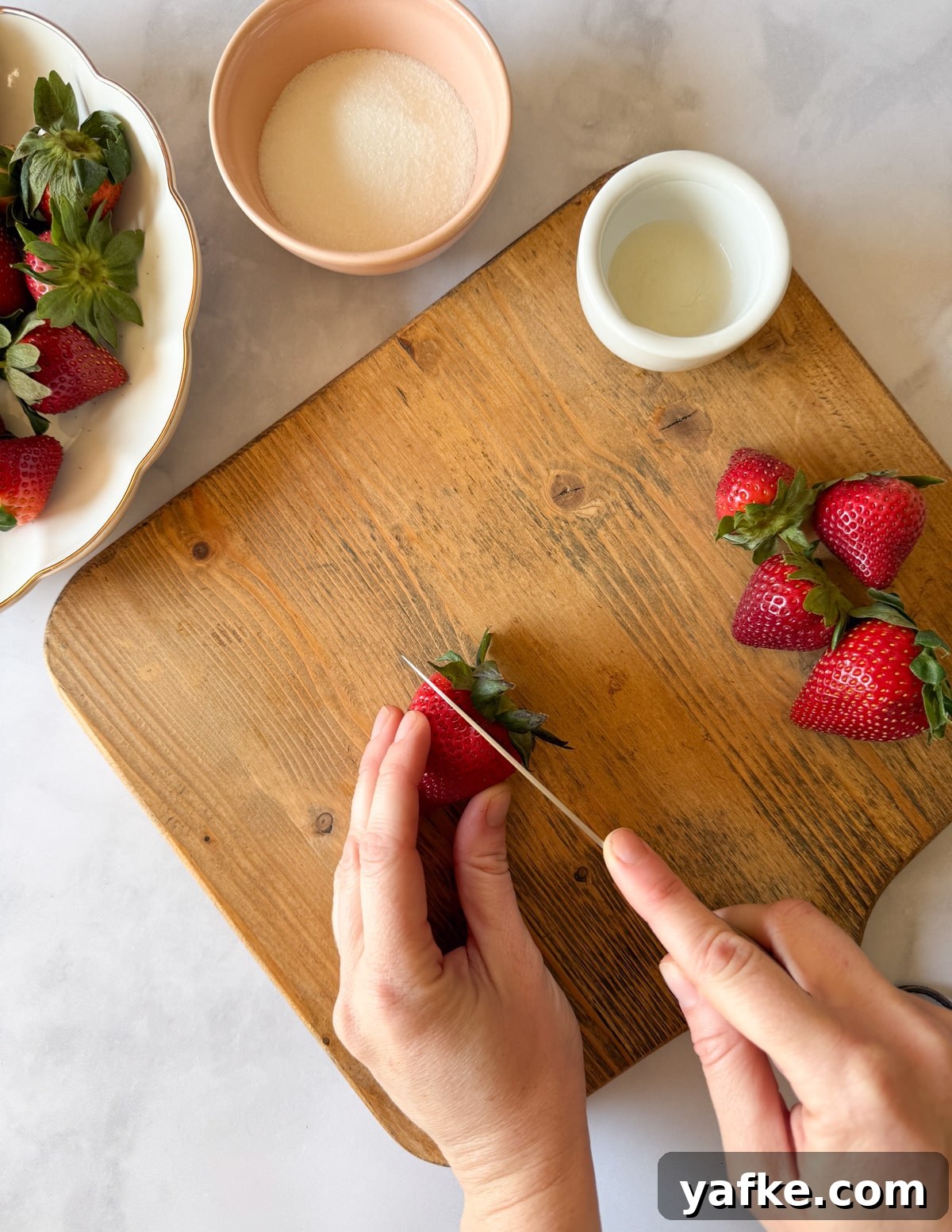 Macerated Strawberries Recipe with Lemon and Vanilla 4 hand cutting the top off of a strawberry