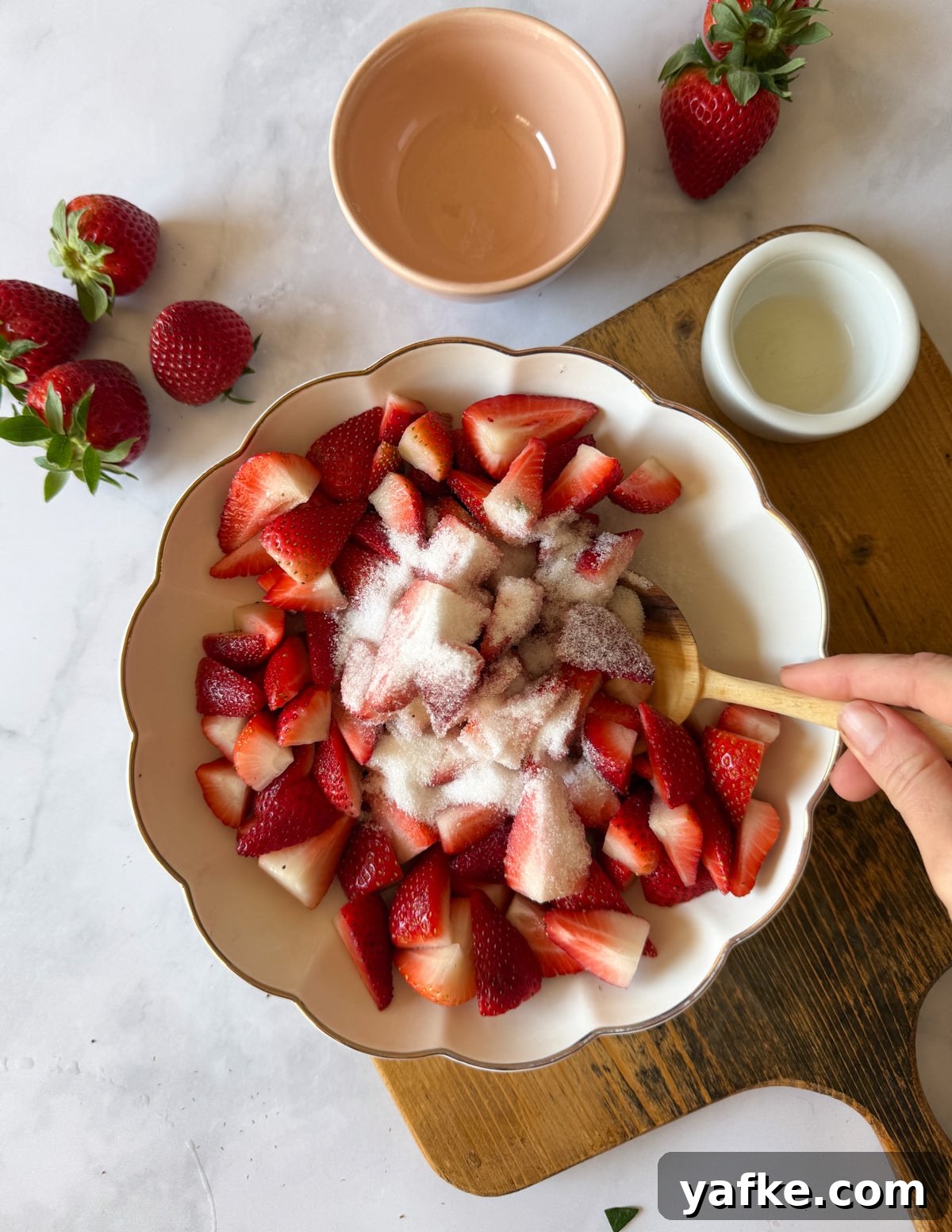 Macerated Strawberries Recipe with Lemon and Vanilla 9 stirring a bowl of quartered strawberries with sugar