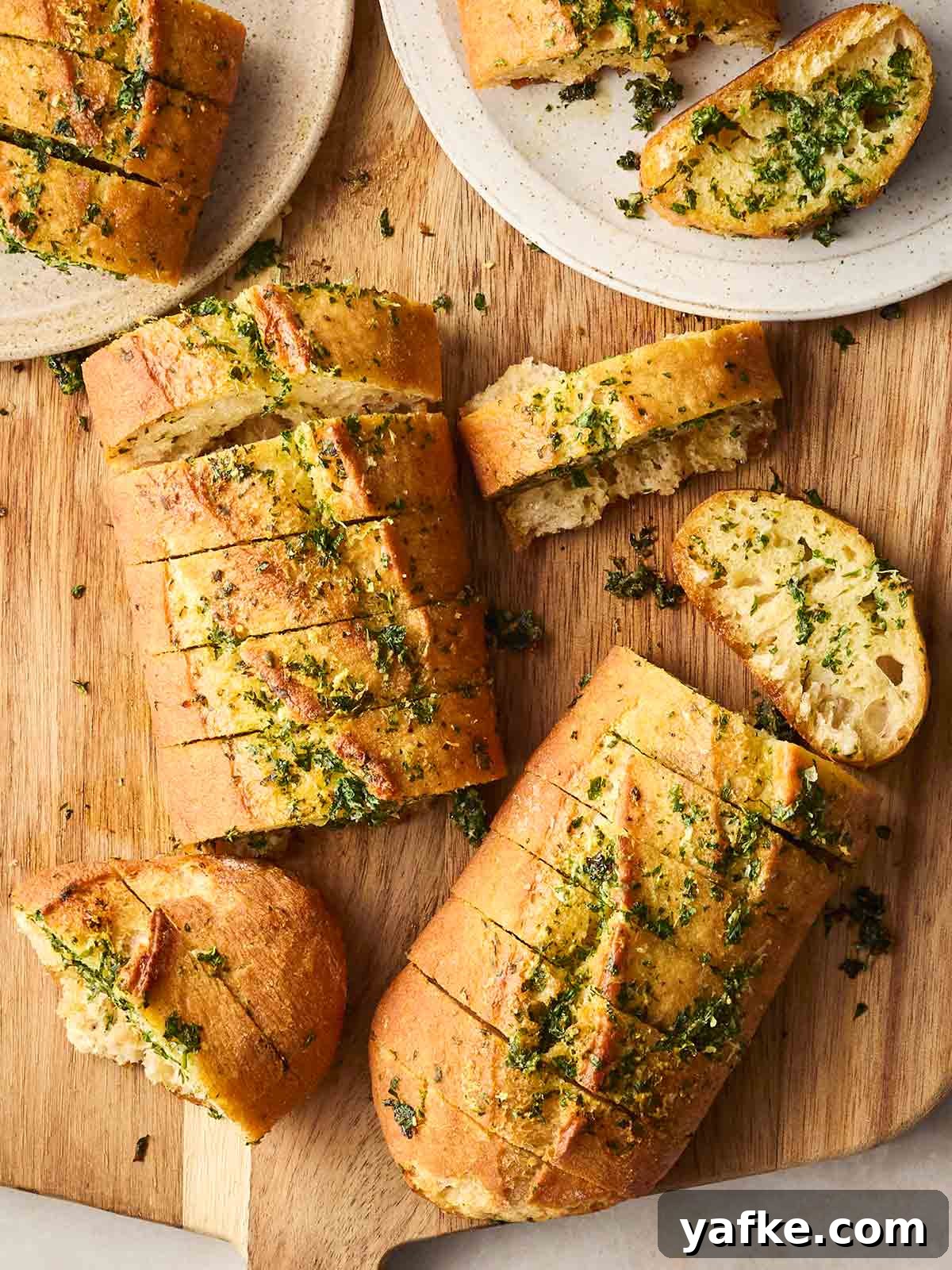 Crispy Garlic Bread Recipe with Herb Butter 3 A bread board filled with sliced homemade garlic bread, with two plates with a couple of pieces on.