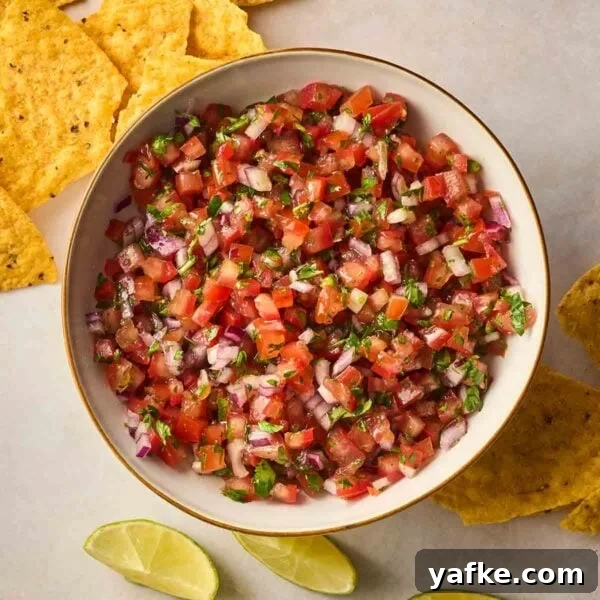 Crispy Garlic Bread Recipe with Herb Butter 7 A bowl filled with fresh Salsa, with tortilla chips and lime wedges on the surface to the side.