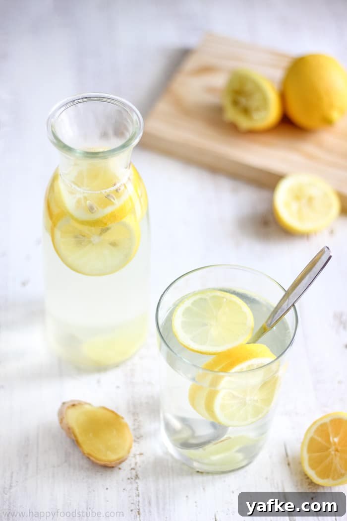 How to Make Lemon Ginger Water: Recipe and Benefits 4 Glass and carafe of infused water with lemon slices, ginger root and a spoon for stirring.