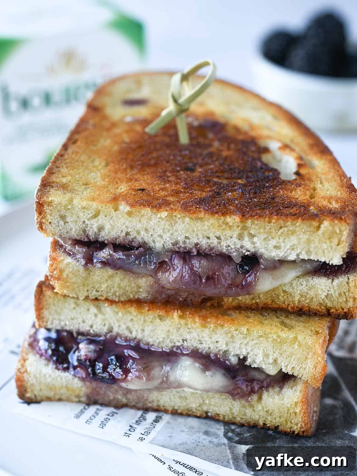 Boursin and Blackberry Grilled Cheese Sandwich 6 Two stacked blackberry grilled cheese sandwiches on a white plate with Boursin cheese in the background.