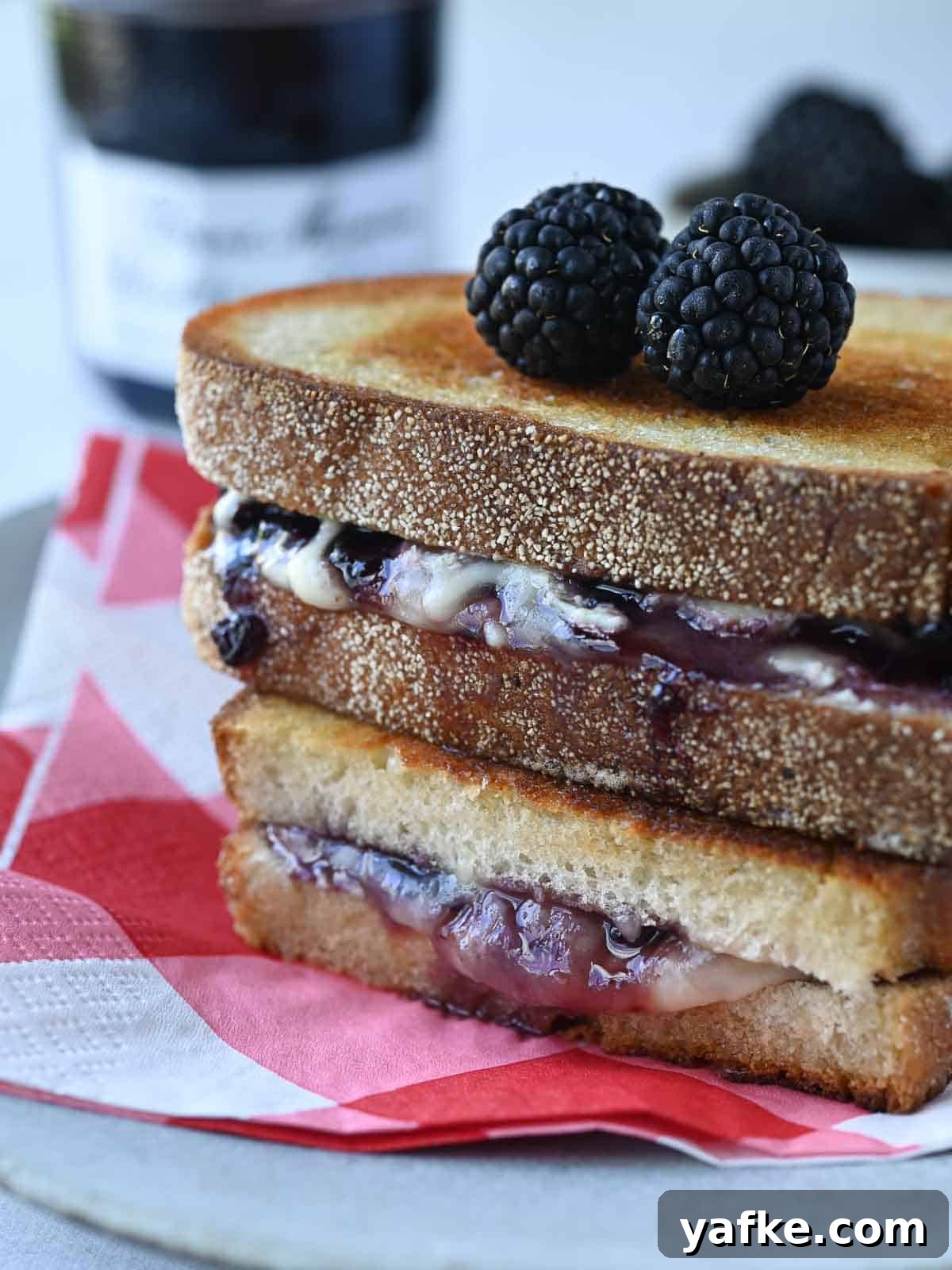 Boursin and Blackberry Grilled Cheese Sandwich 7 Blackberry Boursin grilled cheese stacked on a white plate with a red checkered napkin underneath.