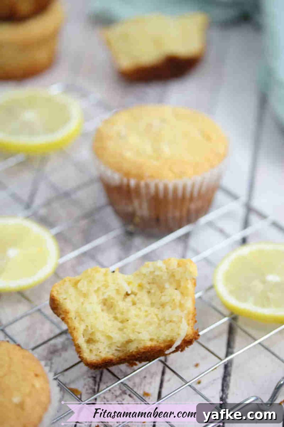 Zesty Gluten Free Lemon Protein Muffins Recipe 8 Lemon protein muffins on a cooling rack with lemons around them and one muffin broken in half.