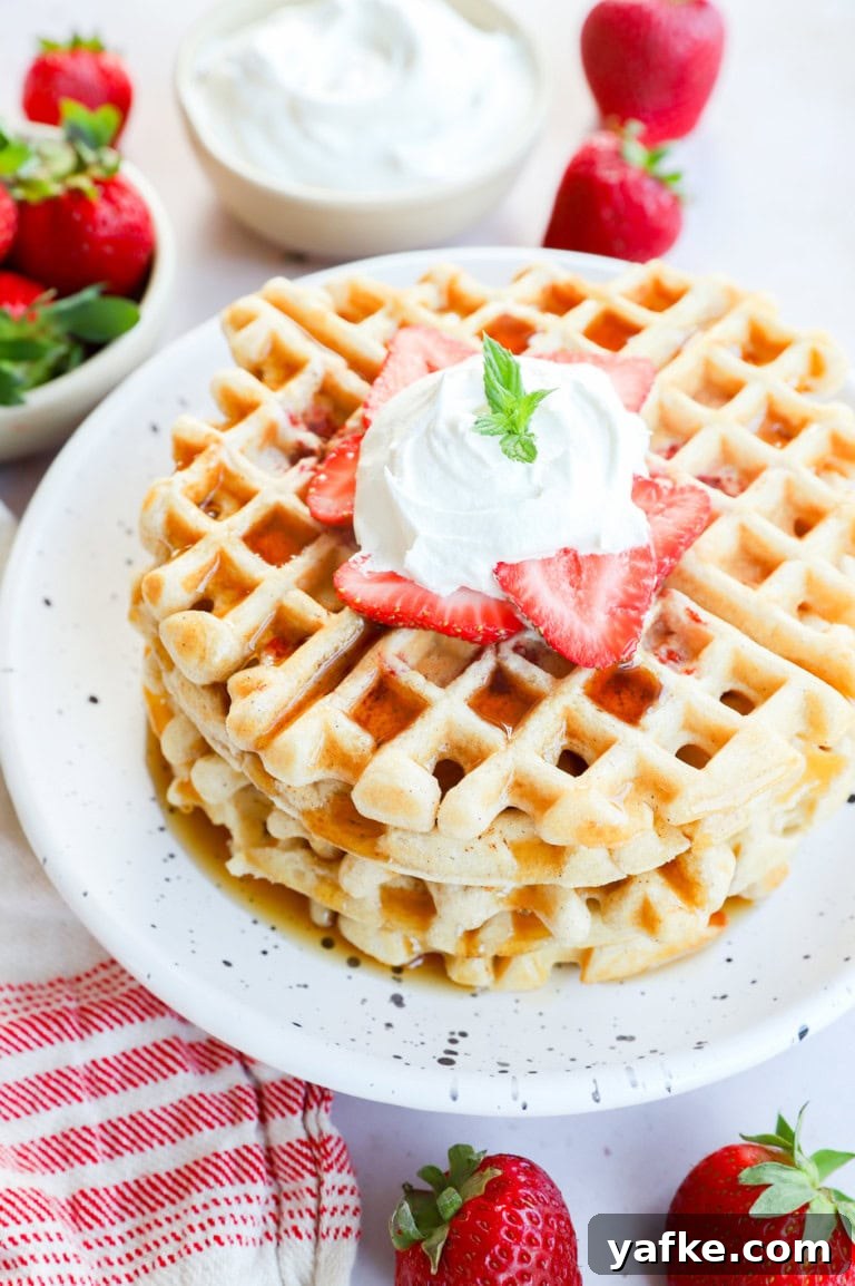 Stack of strawberry waffles with syrup on top