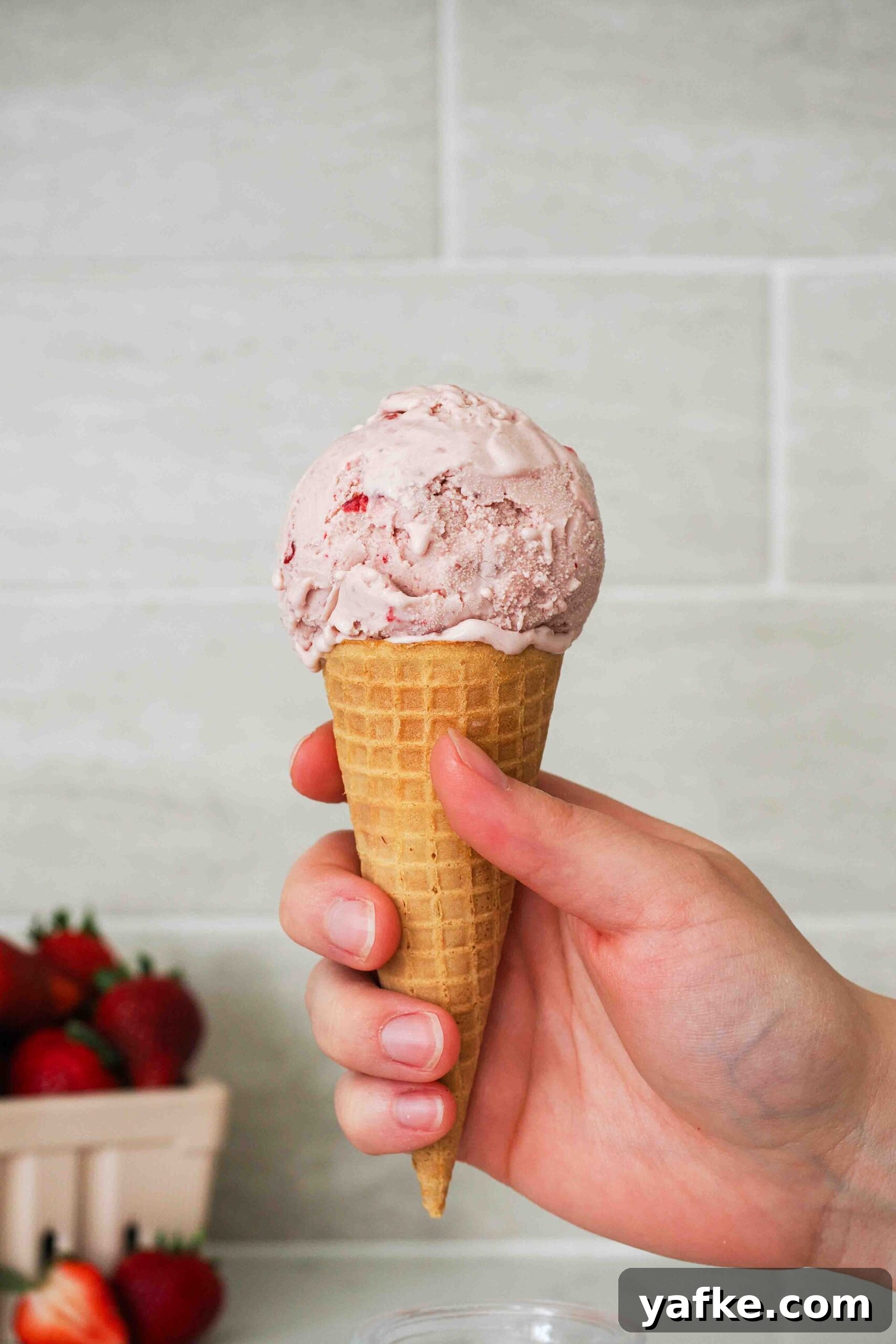 Creamy Homemade Strawberry Ice Cream Recipe 2 A hand holds a strawberry ice cream cone.
