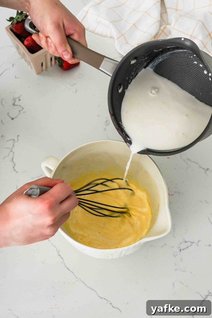 Creamy Homemade Strawberry Ice Cream Recipe 9 Warm cream is poured from a pot into a mixing bowl with ribboned egg yolks.