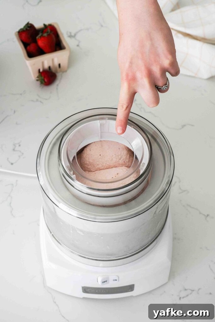 Creamy Homemade Strawberry Ice Cream Recipe 12 A finger points at rounded domes of strawberry frozen custard in an ice cream maker.
