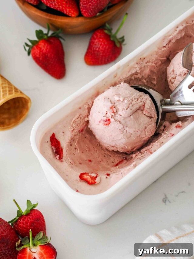 A scoop of strawberry ice cream in a white container.