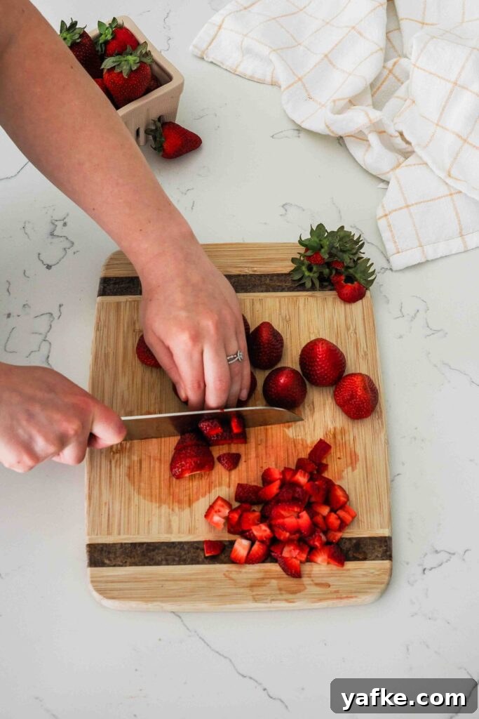 Creamy Homemade Strawberry Ice Cream Recipe 4 A woman dices strawberries on a wooden cutting board.