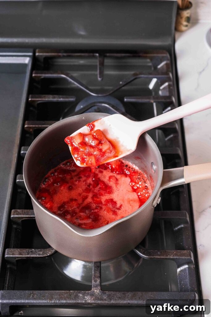Creamy Homemade Strawberry Ice Cream Recipe 6 A spatula holds up strawberry jam over a pot.