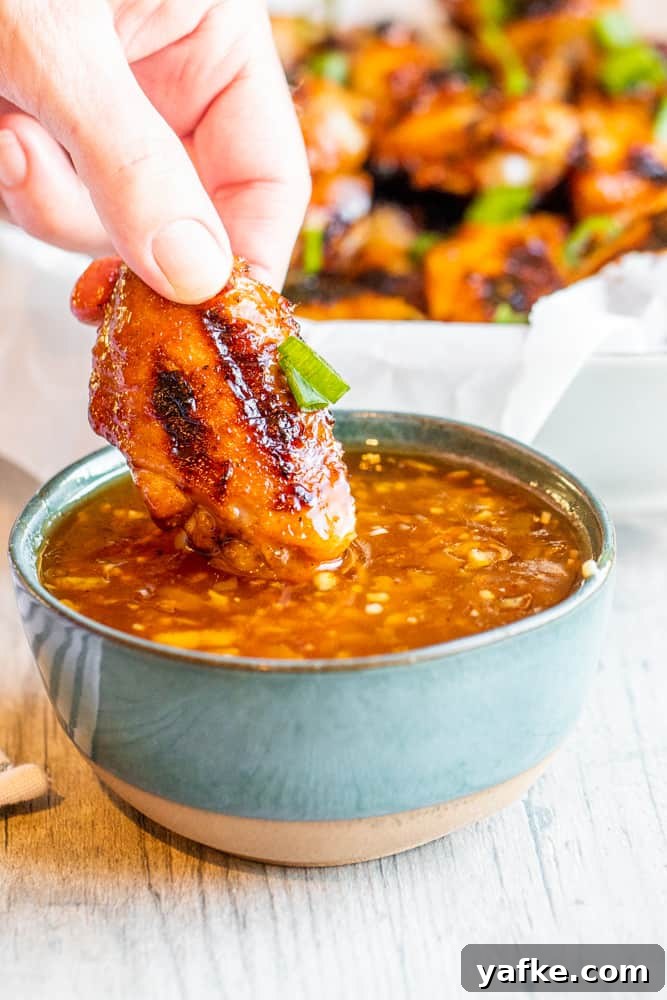 Hand dipping grilled chicken wing into sauce in a blue bowl on a white counter.