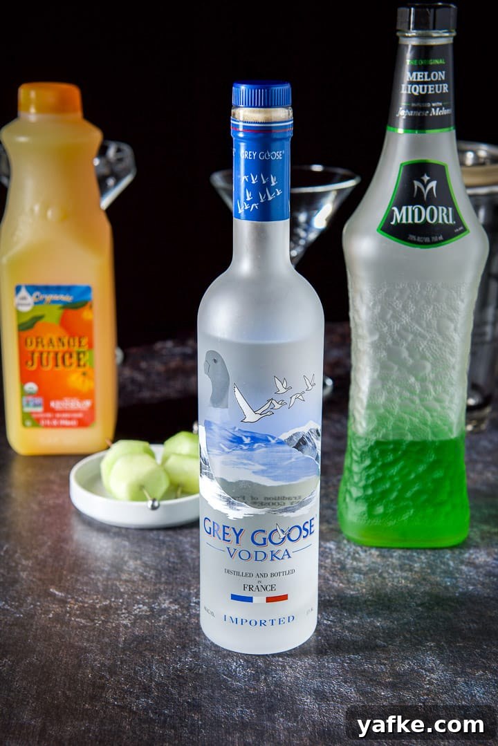 Melon Ball Cocktail Recipe: How to Make the Classic Drink 4 Vodka, Midori, orange juice and melon on a pick with glasses and shaker in the background