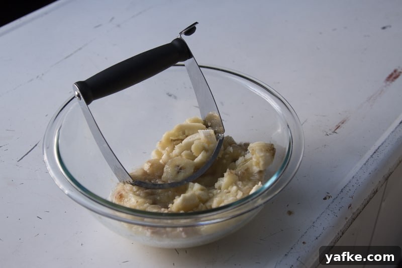 Salted Caramel Pretzel Banana Bread Pudding Recipe 6 Mashed bananas in a glass bowl with a pastry blender.