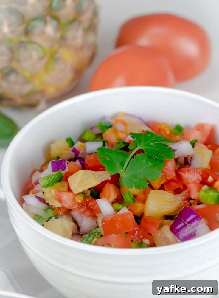 This Pineapple Pico de Gallo is incredibly easy to make, is made with fresh ingredients, and is ready in less than 10 minutes. Pineapple Pico de Gallo in a white bowl and garnished with cilantro.