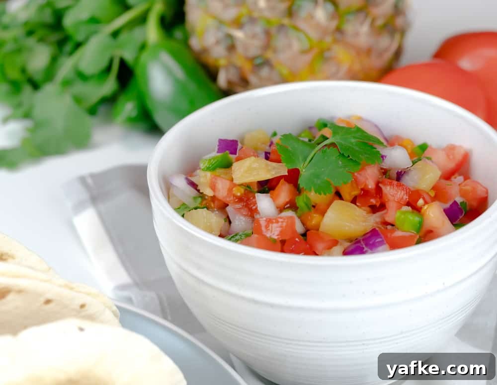 This Pineapple Pico de Gallo is incredibly easy to make, is made with fresh ingredients, and is ready in less than 10 minutes. Pineapple Pico de Gallo served in a white bowl with fresh ingredients on a table.
