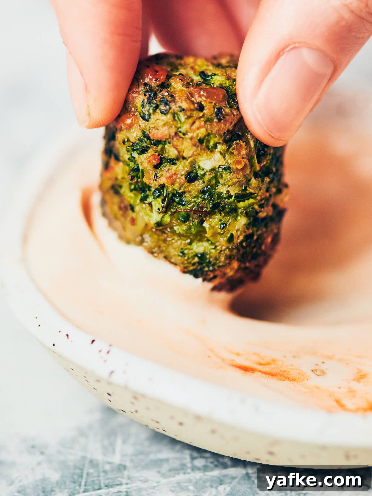Crispy Air Fryer Broccoli Tater Tots 12 A close up of hand holding a brocolli tot being dipped into creamy buffalo sauce