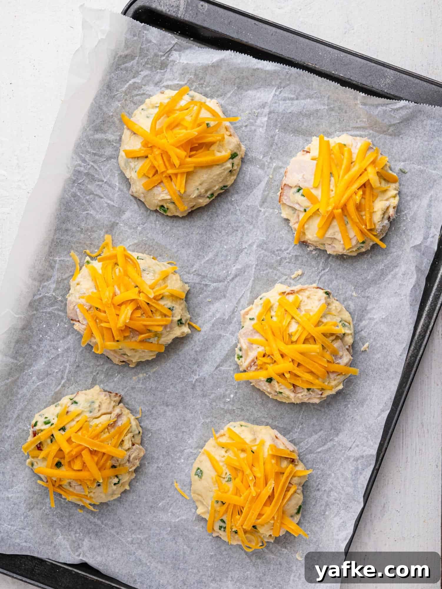 High-Protein Butter-Free Biscuits Recipe 10 Protein biscuits topped with cheese on a baking tray before baking.