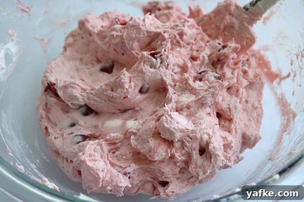 Folding Cherry Fluff Salad ingredients in a bowl.