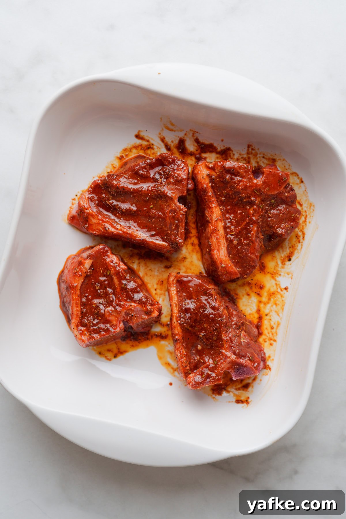 Air Fryer Lamb Chops Recipe with Garlic and Herbs 5 Four marinated pieces of lamb chops served on a white plate.