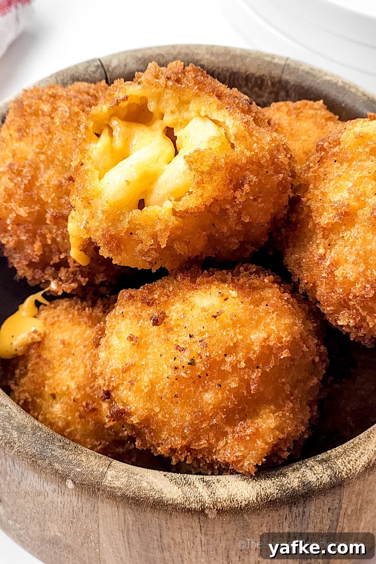 Crispy Fried Mac and Cheese Balls Recipe with Gooey Center 2 fried mac and cheese balls in a bowl, one open showing detail.