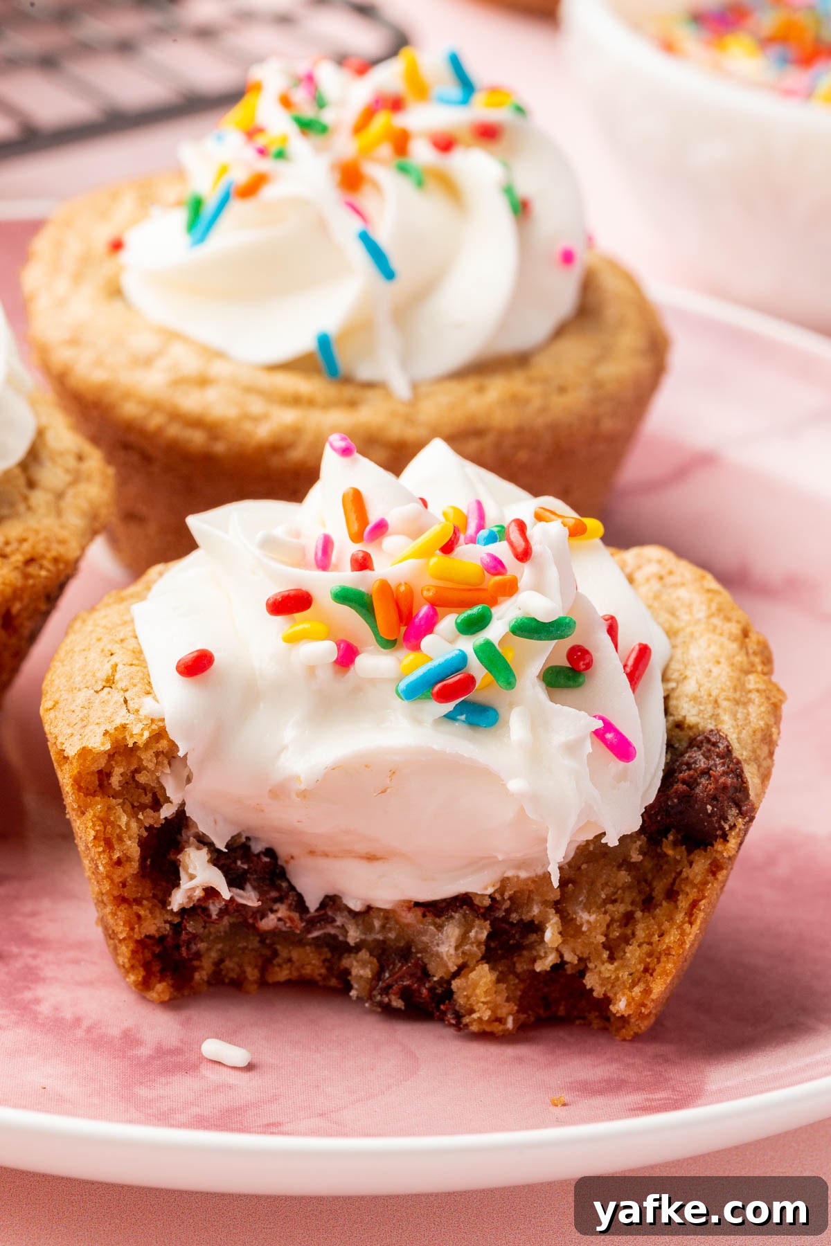 Gluten-Free Chocolate Chip Cookie Cups Recipe 13 A chocolate chip cookie cup filled with vanilla frosting and rainbow sprinkles with a bite taken out.