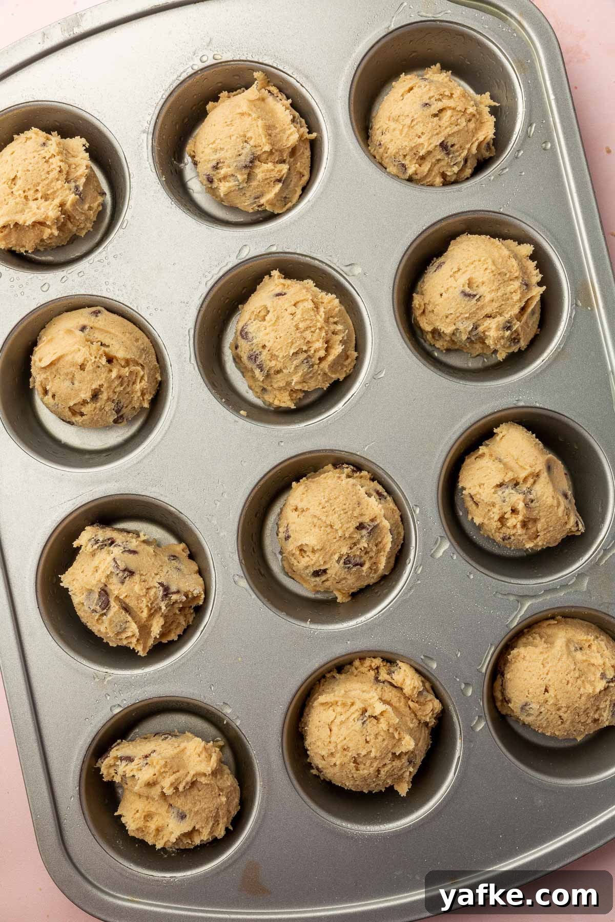 Gluten-Free Chocolate Chip Cookie Cups Recipe 9 Scoops of cookie dough placed in a greased muffin tin.
